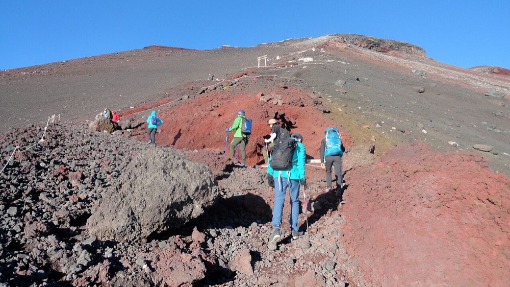 ザック・ストック・レインウェアを身につけて富士山の山頂へ向かう登山者