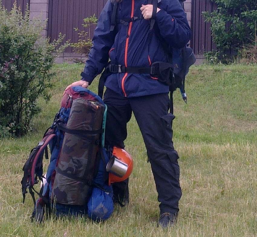 レインウェアを着てザックを背負い、足元に予備の荷物をまとめている登山者