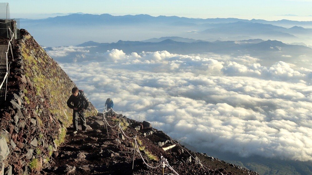 富士山の高所、雲海の上を歩く登山者。早朝の登山道の様子