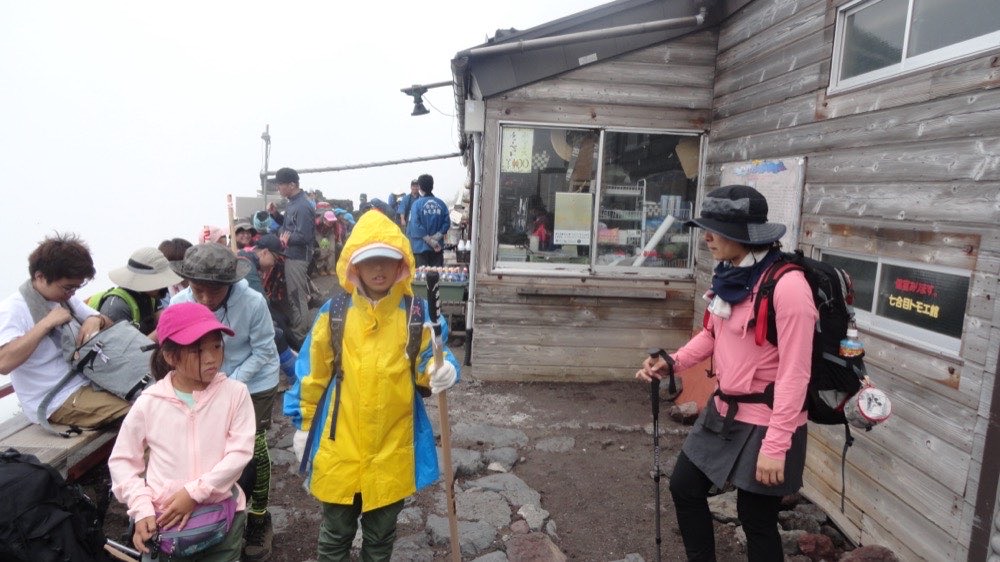 山小屋の前に立つ、防寒着や雨具を着込んだ登山者たち